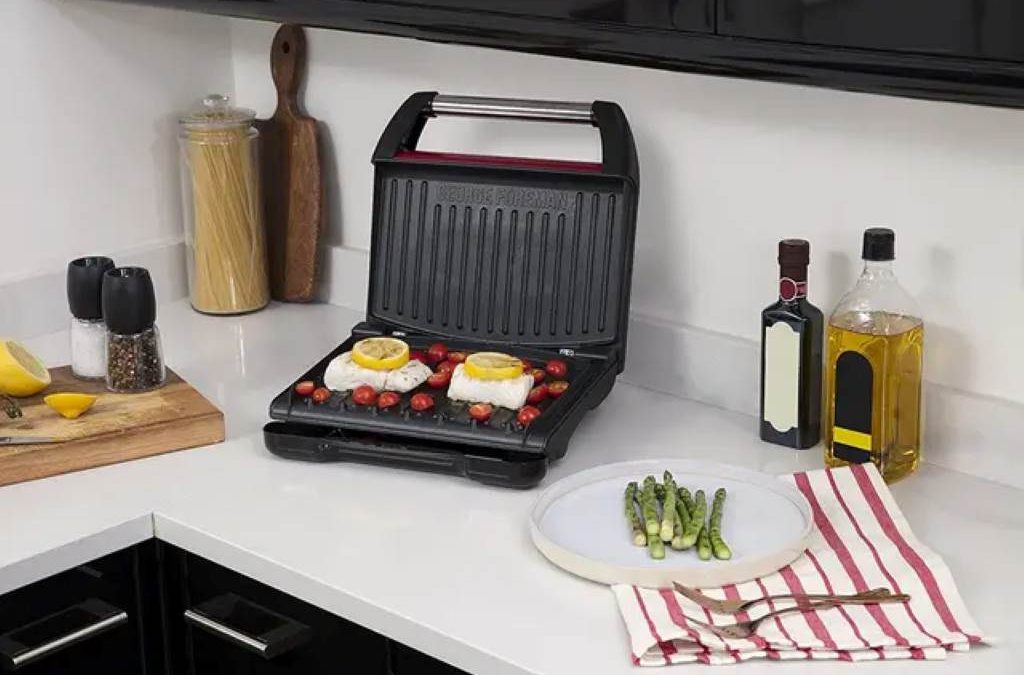 A family smiling in their modern kitchen as they use a George Foreman 4-serving contact grill to cook burgers for dinner