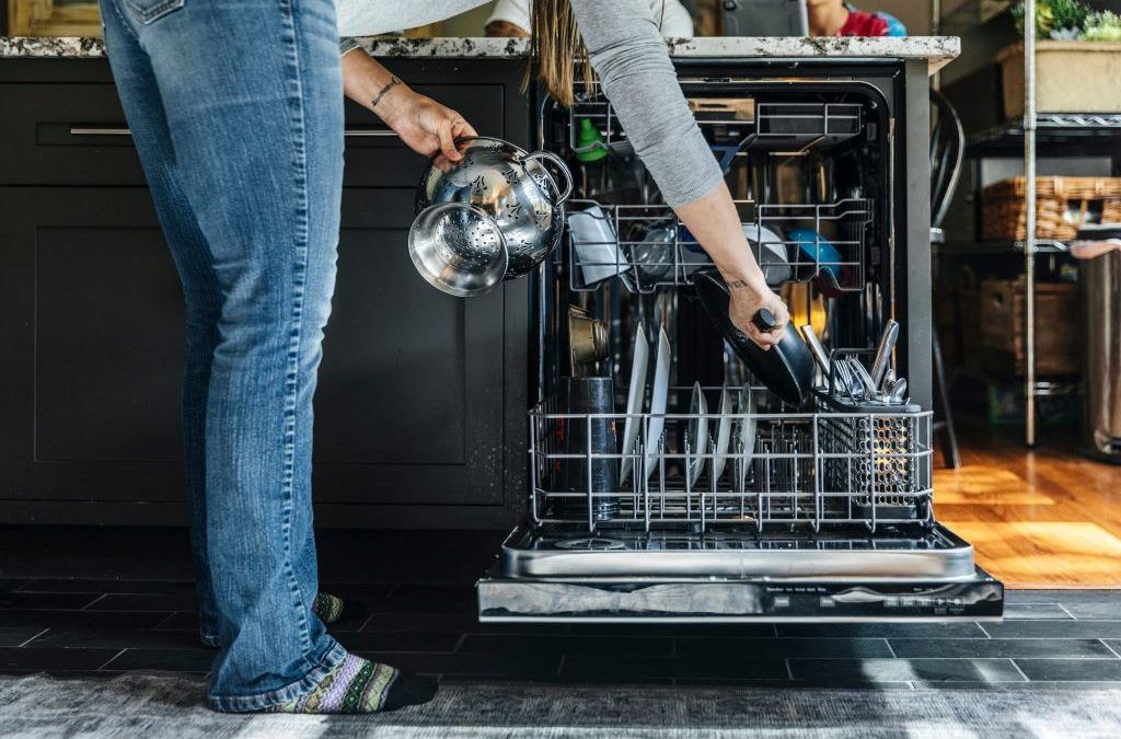 Modern dishwasher running a cleaning cycle with dishes inside kitchen unit.