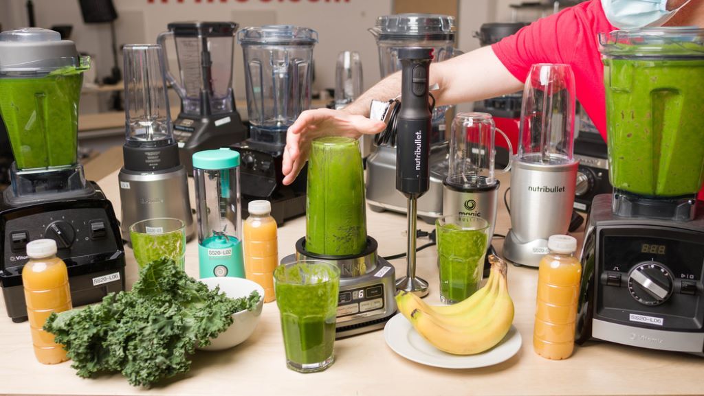 Personal blender with green smoothie beside fresh ingredients on countertop.