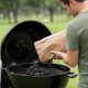 Backyard cook adjusting top lid damper on black Weber Original Kettle grill.