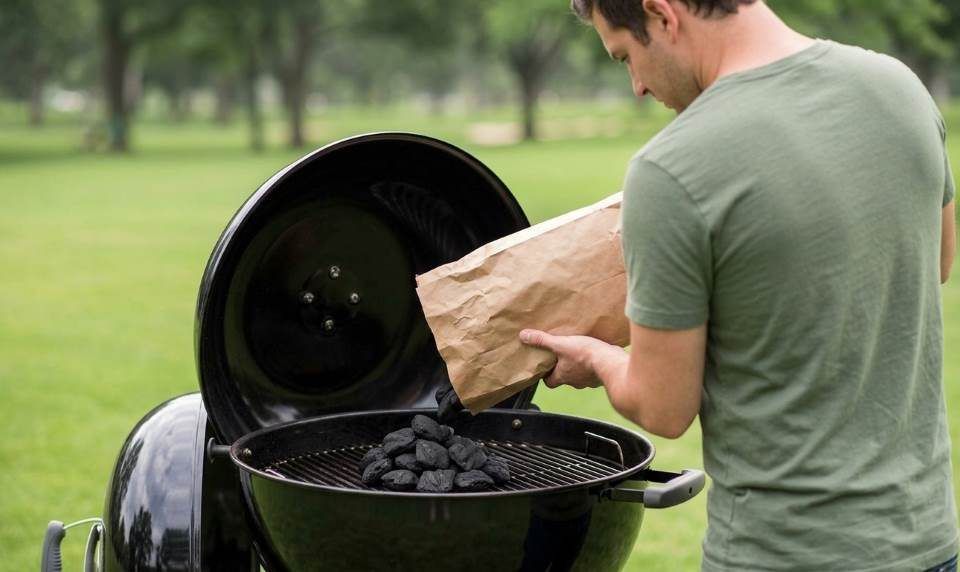 Backyard cook adjusting top lid damper on black Weber Original Kettle grill.