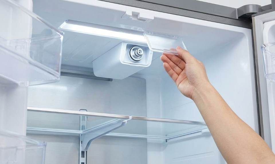 Technician twisting replacement water filter into refrigerator ceiling dock